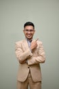 Smiling Asian businessman arms crossed, pointing finger up, stands against an isolated background