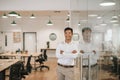 Smiling Asian businessman leaning against a glass wall at work Royalty Free Stock Photo