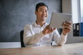 Smiling Asian businessman using a tablet at his office desk Royalty Free Stock Photo