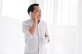 Smiling Asian businessman in white shirt is calling and talking with smartphone. He holding a cup of hot coffee in the morning Royalty Free Stock Photo
