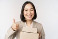 Smiling asian businesswoman, showing thumbs up and boxes with delivery goods, prepare order for client, standing over Royalty Free Stock Photo