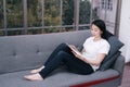 Smiling Asian businesswoman in white shirt is sitting on sofa and reading book in living room at home. Royalty Free Stock Photo