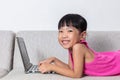 Smiling Asian Chinese little girl laying on sofa using laptop Royalty Free Stock Photo