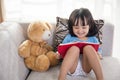 Smiling Asian Chinese little girl reading book with teddy bear Royalty Free Stock Photo