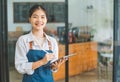 Smiling Asian coffee shop owner standing in front of cashier counter with tablet ready to take menu orders.welcome customers who