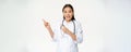 Smiling asian doctor, female healthcare worker pointing at upper left corner, looking amazed, showing medical Royalty Free Stock Photo