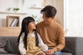 Smiling Asian father embracing daughter sitting on couch, posing for family photo indoors. Happy young dad with little child girl Royalty Free Stock Photo