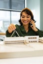 Smiling asian female architect talking on smart phone measuring architectural model in office Royalty Free Stock Photo