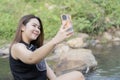Smiling Asian female taking selfie by smartphone along sunny summer stream Royalty Free Stock Photo