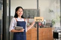 Smiling Asian female waitres stands at the front door with a digital tablet in her hand