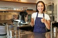 Smiling asian girl barista, cafe owner in apron, showing card machine, payment reader, taking contactless orders in her Royalty Free Stock Photo