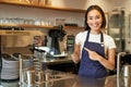 Smiling asian girl barista, cafe owner in apron, showing card machine, payment reader, taking contactless orders in her Royalty Free Stock Photo