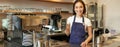 Smiling asian girl barista, cafe owner in apron, showing card machine, payment reader, taking contactless orders in her Royalty Free Stock Photo
