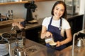 Smiling asian girl barista, cafe staff pouring steamed milk in coffee, prepare cappuccino with latte art, standing in Royalty Free Stock Photo