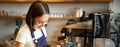 Smiling asian girl barista, cafe staff pouring steamed milk in coffee, prepare cappuccino with latte art, standing in Royalty Free Stock Photo