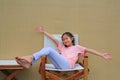 Smiling Asian girl child open hands outstretched and relaxing on wood chair against cement wall background Royalty Free Stock Photo