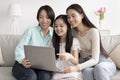 Smiling Asian girl with her mom and granny watching video, searching internet on laptop in living room Royalty Free Stock Photo