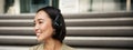 Smiling asian girl, laughing, listening music in headphones, sitting outdoors. Uni student enjoying free time Royalty Free Stock Photo