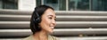 Smiling asian girl, laughing, listening music in headphones, sitting outdoors. Uni student enjoying free time Royalty Free Stock Photo