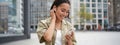 Smiling asian girl listens music in wireless headphones, looks at her phone, choosing music or podcast. Young woman Royalty Free Stock Photo