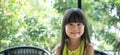 Smiling asian girl sitting on a chair looking at a camera with green background behind. Portrait adorable asian girl with smiling Royalty Free Stock Photo