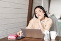 Smiling asian girl student, woman sitting with laptop at home kitchen, browing smartphone social media and resting