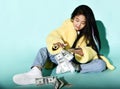 Smiling asian girl in stylish yellow fur coat, jeans and sneakers sitting on floor and counting hundreds of dollars cash Royalty Free Stock Photo