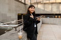 Smiling asian girl using smartphone and drinking coffee while standing near subway Royalty Free Stock Photo