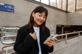 Smiling asian girl using smartphone while standing near subway Royalty Free Stock Photo