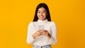 Smiling asian girl using smartphone on yellow background Royalty Free Stock Photo