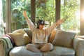 Smiling asian girl wearing vr headset with arms outstretched sitting on sofa