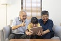 Smiling Asian grandparents on couch with granddaughter looking at tablet. happy three generation family spending time together at Royalty Free Stock Photo