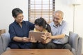 Smiling Asian grandparents on couch with granddaughter looking at tablet. happy three generation family spending time together at Royalty Free Stock Photo