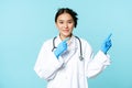 Smiling asian healthcare worker, wearing sterile gloves and uniform, pointing right, demonstrating chart, hospital Royalty Free Stock Photo