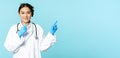 Smiling asian healthcare worker, wearing sterile gloves and uniform, pointing right, demonstrating chart, hospital Royalty Free Stock Photo