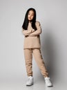 Smiling asian kid girl in green casual sportswear cotton pants, hoodie, jersey and sneakers stands holding arms crossed