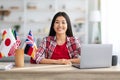 Smiling Asian Lady Sitting At Table With International Flags And Laptop Royalty Free Stock Photo