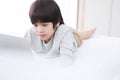 Smiling Asian little boy is studying and doing homework or playing game with laptop in bedroom. Homeschool and quarantine during Royalty Free Stock Photo