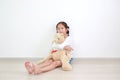 Smiling asian little child girl hugging a teddy bear doll sitting against white wall in the room Royalty Free Stock Photo