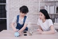 Smiling Asian little asian girl child is putting coins and banknote into piggy bank for saving money for the future with mother on Royalty Free Stock Photo