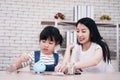 Smiling Asian little asian girl child is putting coins into piggy bank for saving money for the future with mother on wooden table Royalty Free Stock Photo