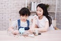 Smiling Asian little asian girl child is putting coins into piggy bank for saving money for the future with mother on wooden table Royalty Free Stock Photo