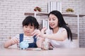 Smiling Asian little asian girl child is putting coins into piggy bank for saving money for the future with mother on wooden table Royalty Free Stock Photo