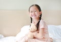 Smiling Asian little girl cuddle teddy bear sitting on the bed at home