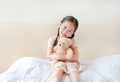 Smiling Asian little girl cuddle teddy bear sitting on the bed at home