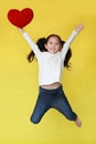 Smiling asian little girl jumping on air with holding red heart in hand isolated on yellow background Royalty Free Stock Photo