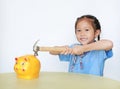 Smiling Asian little girl in school uniform breaking piggy bank isolated on white background at table. Schoolgirl with Money Royalty Free Stock Photo