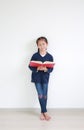 Smiling asian little kid girl in school uniform reading a book and standing against white wall in the room Royalty Free Stock Photo
