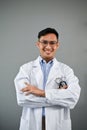 Smiling Asian male doctor standing on an isolated grey background with his arms crossed Royalty Free Stock Photo