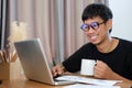 Smiling asian man holding coffee cup and using laptop computer at home Royalty Free Stock Photo